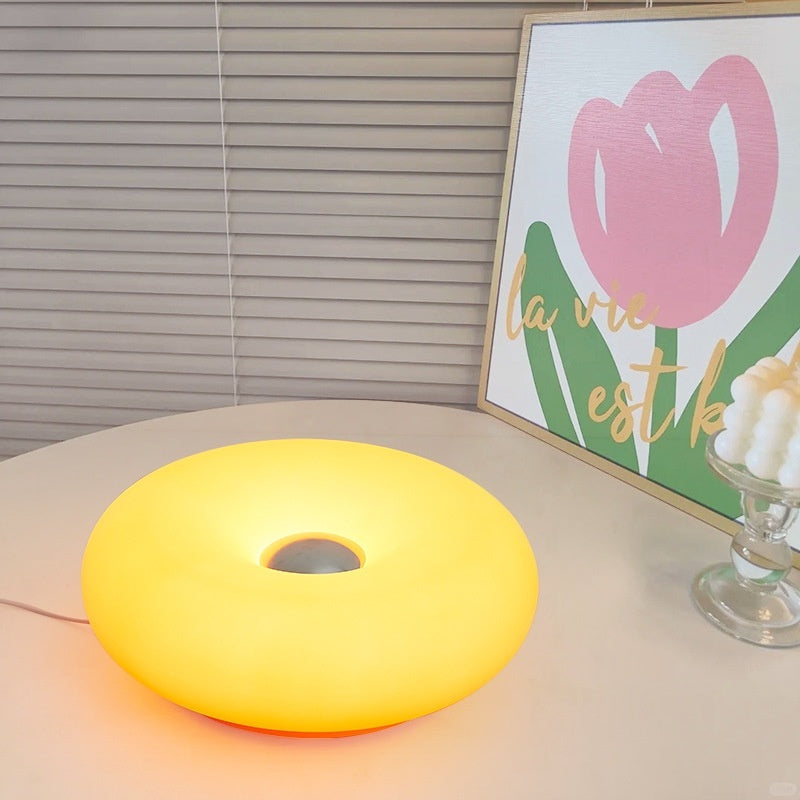 Moodly Puff donut lamp glowing yellow on a round table