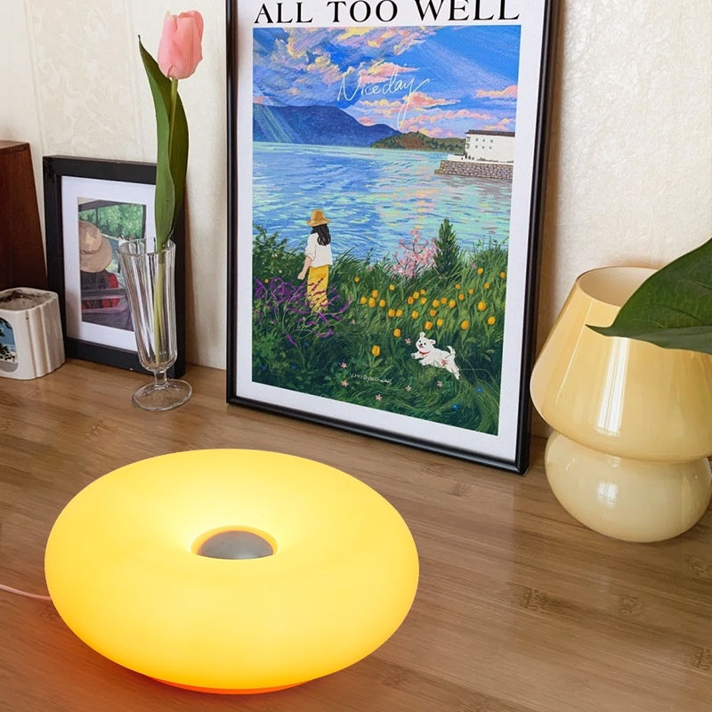 Moodly Puff donut lamp glowing on a wooden sideboard next to a framed picture